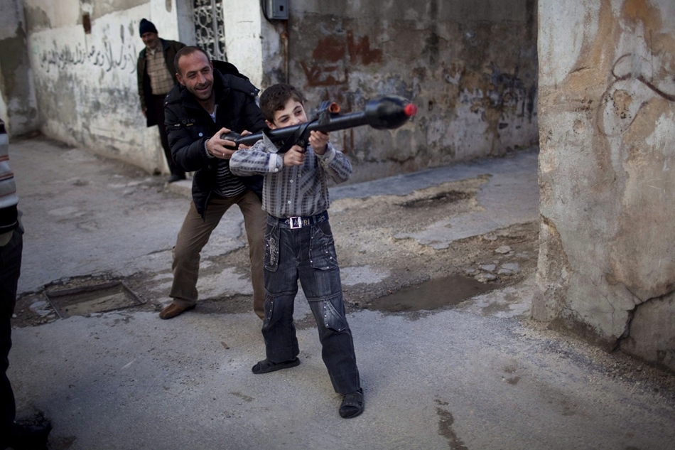 Szír férfi tanítja játék RPG rakétagránát-vető használatára 11 éves fiát.